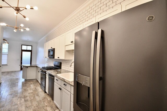 kitchen featuring a chandelier, a sink, black appliances, tasteful backsplash, and crown molding