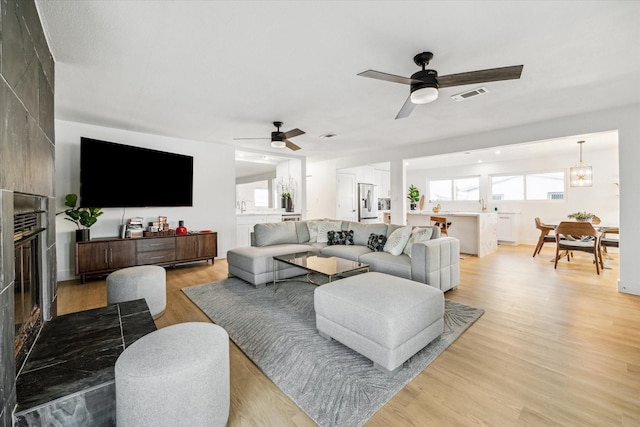 living room featuring sink, light hardwood / wood-style floors, a large fireplace, and ceiling fan