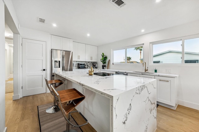 kitchen with a kitchen island, a breakfast bar, white cabinetry, sink, and stainless steel refrigerator with ice dispenser