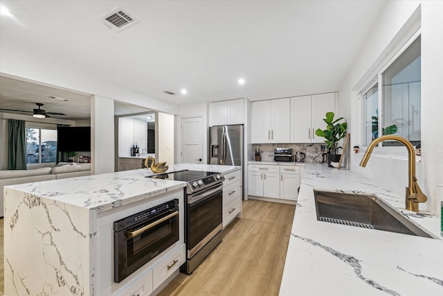 kitchen featuring sink, white cabinetry, light wood-type flooring, stainless steel appliances, and light stone countertops