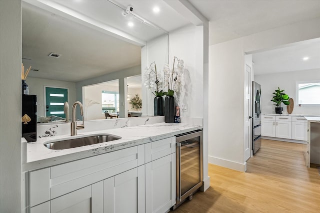 kitchen with sink, stainless steel fridge, wine cooler, light stone counters, and white cabinets