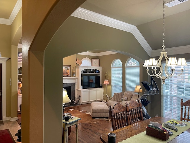 living room with a tiled fireplace, an inviting chandelier, ornamental molding, vaulted ceiling, and hardwood / wood-style floors