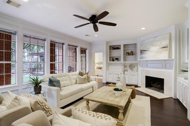 living room with crown molding, a premium fireplace, ceiling fan, dark hardwood / wood-style flooring, and built in shelves