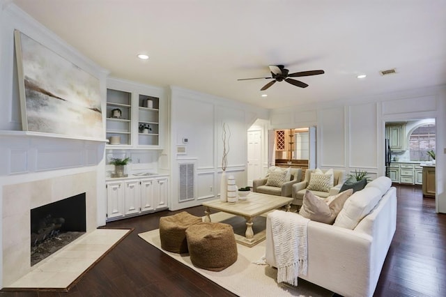 living room featuring ceiling fan, dark hardwood / wood-style floors, built in features, and a fireplace