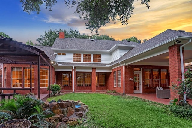 back house at dusk featuring a pergola, a patio area, and a lawn