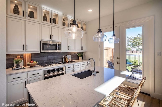 kitchen featuring decorative light fixtures, white cabinetry, sink, stainless steel appliances, and light stone countertops