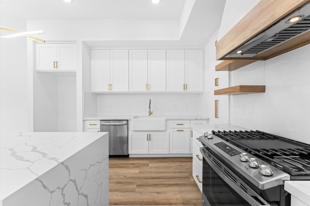 kitchen featuring premium range hood, sink, white cabinetry, appliances with stainless steel finishes, and light stone countertops