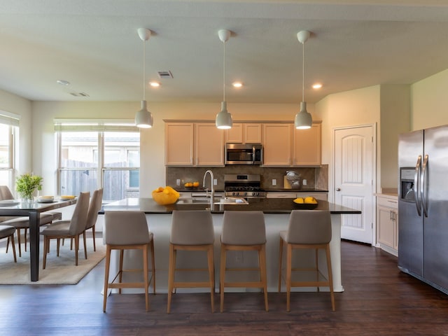 kitchen featuring stainless steel appliances, hanging light fixtures, and a center island with sink