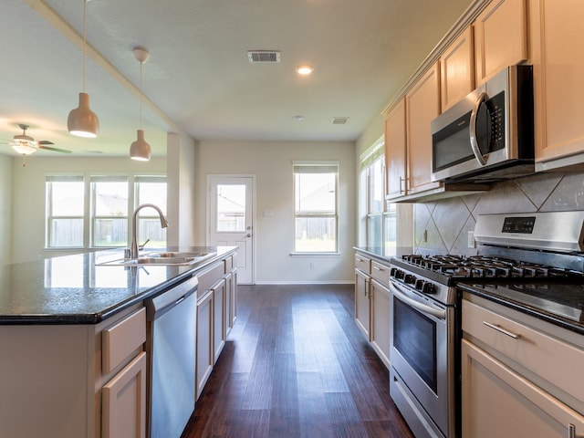 kitchen featuring sink, dark stone counters, decorative backsplash, a kitchen island with sink, and stainless steel appliances