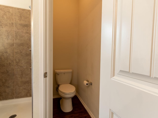 bathroom with tiled shower, toilet, and hardwood / wood-style floors