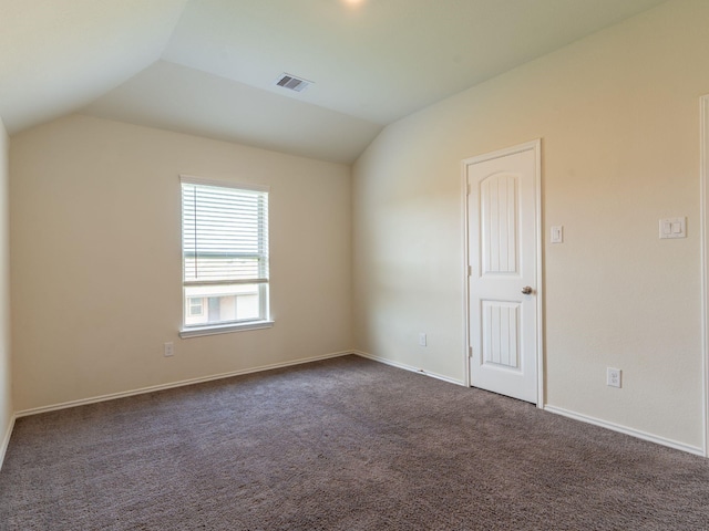 spare room featuring dark colored carpet and lofted ceiling