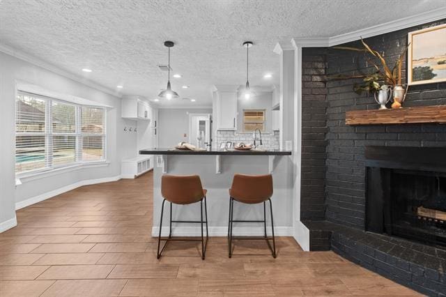 kitchen with a breakfast bar area, white cabinetry, tasteful backsplash, a fireplace, and decorative light fixtures