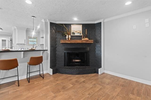 kitchen featuring crown molding, a brick fireplace, white cabinets, and light wood-type flooring