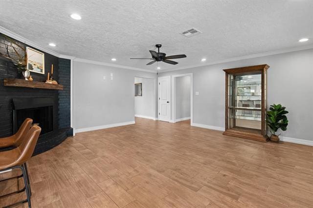 living room with crown molding, a brick fireplace, a textured ceiling, and light hardwood / wood-style floors