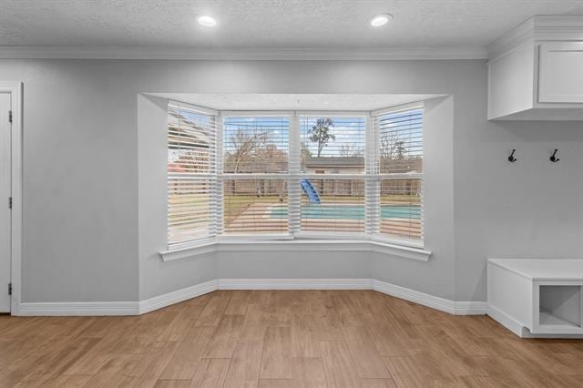 unfurnished dining area featuring crown molding, a textured ceiling, and light wood-type flooring