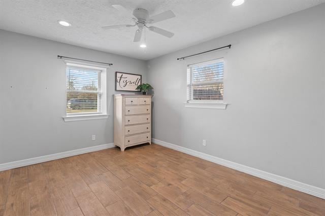 empty room featuring ceiling fan, plenty of natural light, light hardwood / wood-style floors, and a textured ceiling