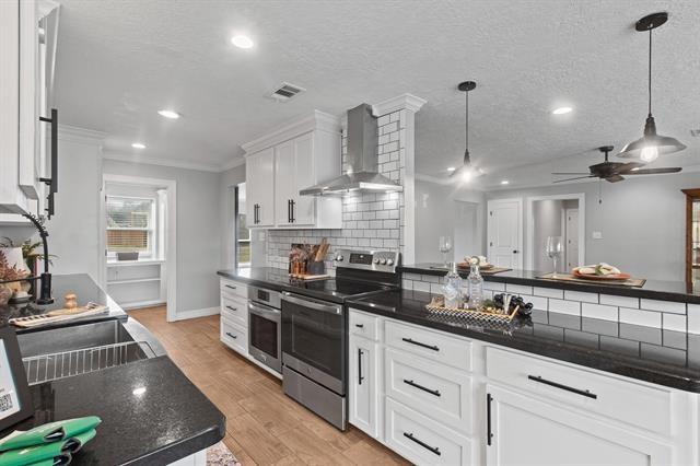 kitchen with wall chimney exhaust hood, pendant lighting, stainless steel appliances, light hardwood / wood-style floors, and white cabinets