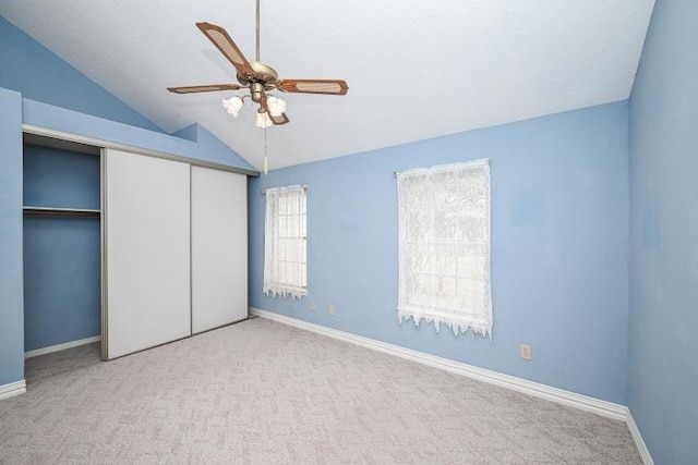 unfurnished bedroom featuring baseboards, vaulted ceiling, a closet, and light carpet