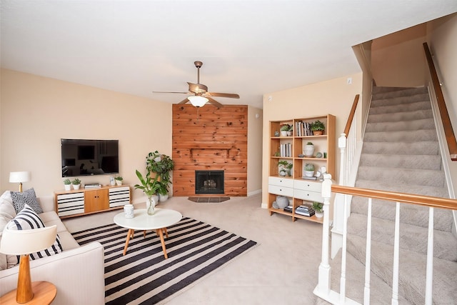 carpeted living area with stairway, a fireplace with raised hearth, and a ceiling fan