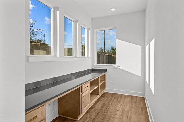 unfurnished office featuring wood finished floors, built in desk, baseboards, and recessed lighting