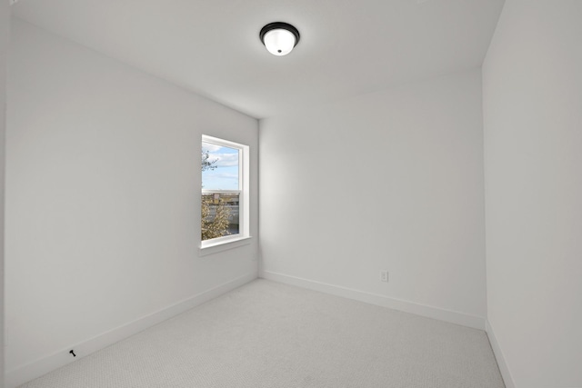 spare room featuring light colored carpet and baseboards