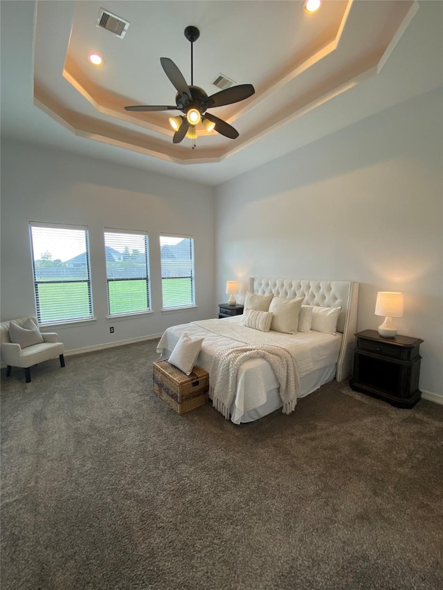 carpeted bedroom featuring a raised ceiling, ceiling fan, and multiple windows