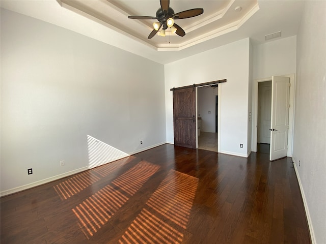 unfurnished bedroom featuring dark hardwood / wood-style floors, a towering ceiling, ceiling fan, a raised ceiling, and a barn door