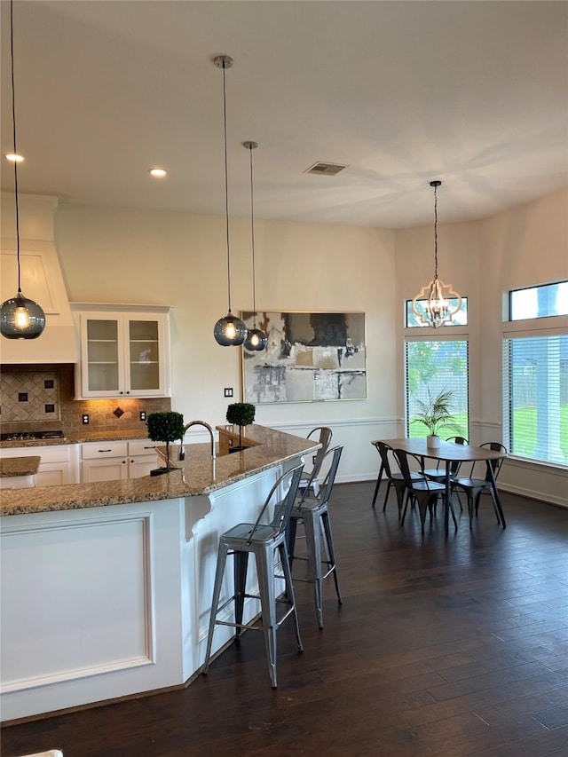 kitchen featuring stone counters, white cabinets, a kitchen bar, hanging light fixtures, and gas stovetop