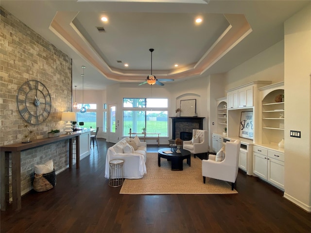 living room featuring dark hardwood / wood-style floors, a multi sided fireplace, a tray ceiling, and ceiling fan