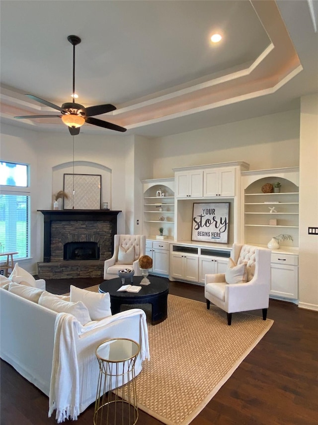 living room featuring a tray ceiling, a stone fireplace, dark hardwood / wood-style floors, and ceiling fan