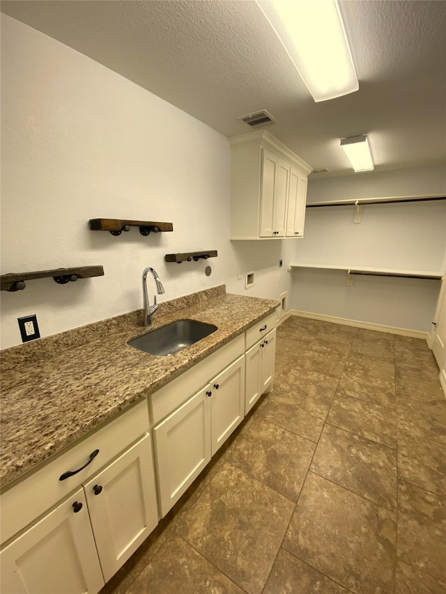 kitchen with light stone counters, sink, a textured ceiling, and white cabinets