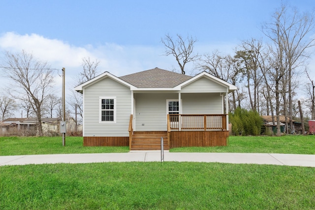 view of front facade featuring covered porch, roof with shingles, and a front yard