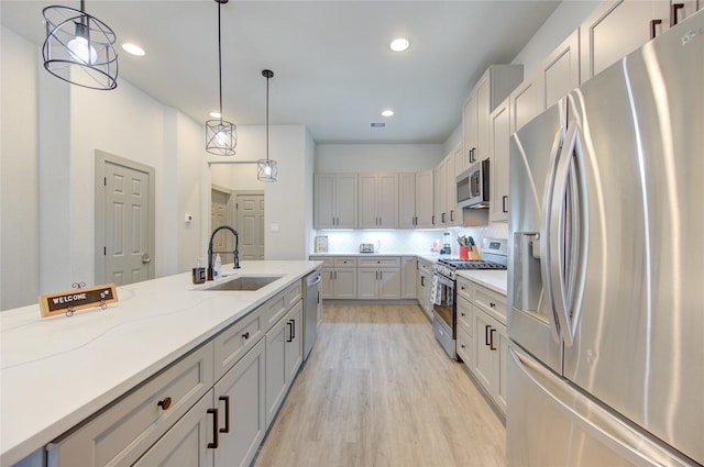 kitchen with sink, pendant lighting, stainless steel appliances, light stone countertops, and light hardwood / wood-style floors