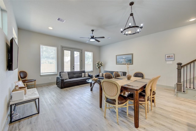 dining space with french doors, ceiling fan with notable chandelier, and light wood-type flooring