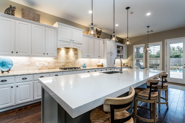 kitchen featuring white cabinetry, sink, dark hardwood / wood-style flooring, hanging light fixtures, and a kitchen island with sink