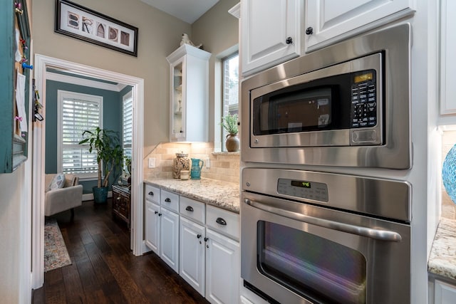 kitchen featuring plenty of natural light, stainless steel microwave, white cabinets, decorative backsplash, and light stone countertops