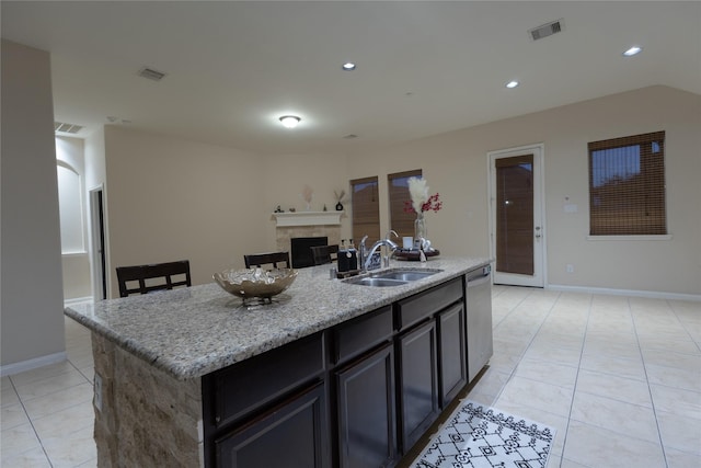 kitchen featuring a tile fireplace, sink, light tile patterned floors, light stone counters, and a center island with sink