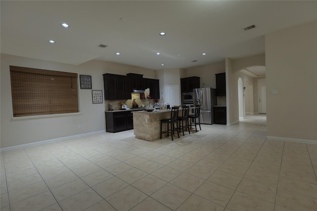 kitchen featuring light tile patterned flooring, appliances with stainless steel finishes, a kitchen breakfast bar, decorative backsplash, and a kitchen island with sink