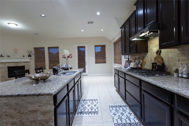 kitchen with stainless steel gas cooktop, sink, light stone counters, a kitchen island with sink, and backsplash