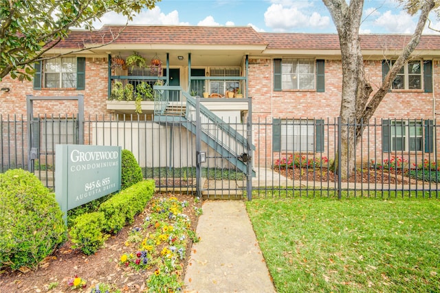 view of property with a fenced front yard, stairway, a front lawn, and brick siding