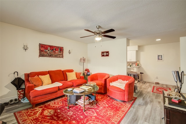 living area with light wood-style floors, ceiling fan, baseboards, and a textured ceiling