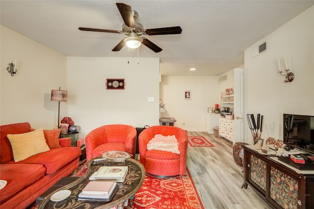 living room featuring a textured ceiling, a ceiling fan, visible vents, and light wood-style floors