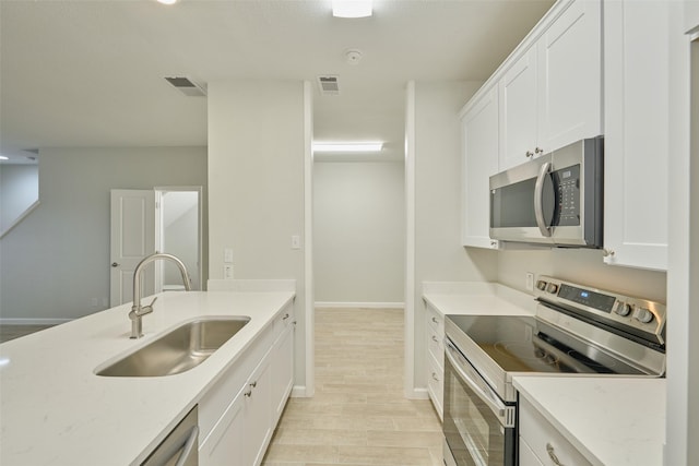 kitchen with stainless steel appliances, white cabinetry, light stone countertops, and sink