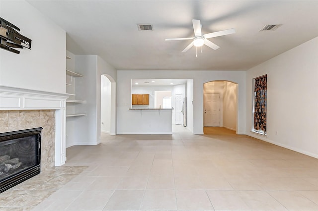 unfurnished living room featuring ceiling fan, light tile patterned floors, a fireplace, and built in shelves