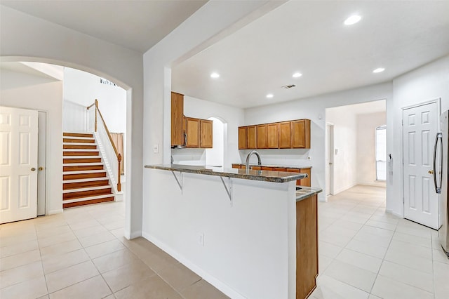 kitchen with light tile patterned floors, kitchen peninsula, a kitchen breakfast bar, and dark stone counters