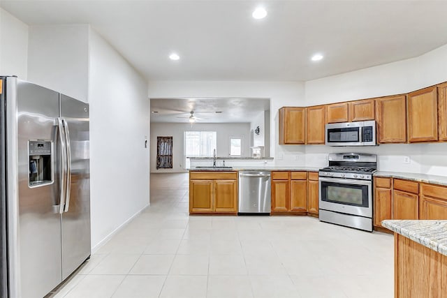 kitchen with appliances with stainless steel finishes, sink, light tile patterned floors, ceiling fan, and light stone counters