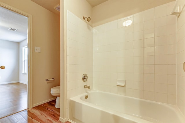 bathroom featuring hardwood / wood-style flooring, tiled shower / bath combo, and toilet