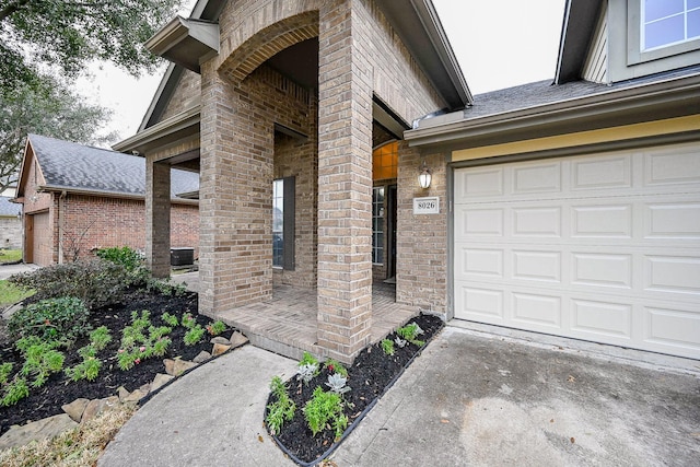 doorway to property with a shingled roof, concrete driveway, and brick siding