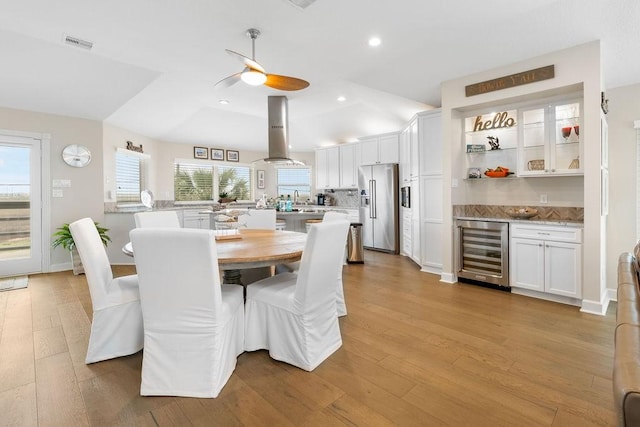 dining area featuring wet bar, light hardwood / wood-style flooring, ceiling fan, and beverage cooler