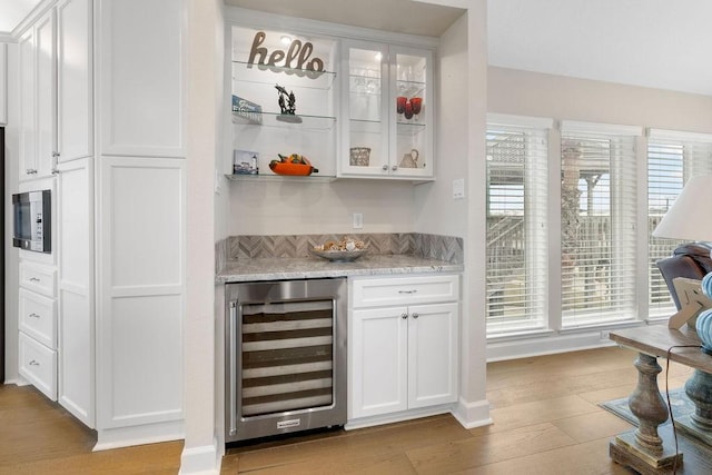 bar featuring plenty of natural light, light stone countertops, white cabinets, and wine cooler